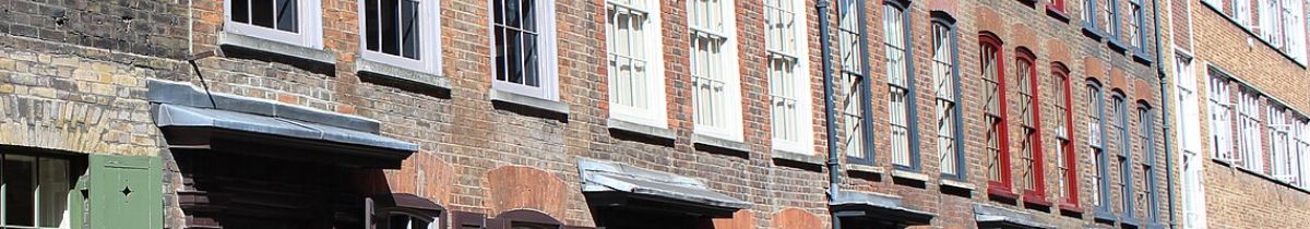 Upper floors of a brick terrace with sash windows and painted shopfront awnings below